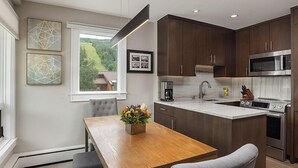 A modern kitchen with dark wood cabinets, a central island, stainless steel appliances, and a view of greenery outside. - Vail 21 407 - 2 Bedroom Diamond (Vail)