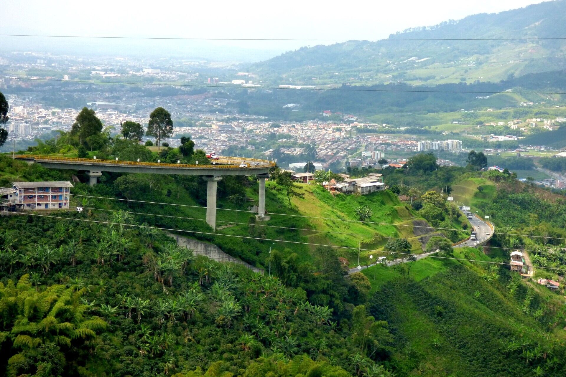 A bridge with a road passing over a lush green area, leading to a cityscape in the distance.