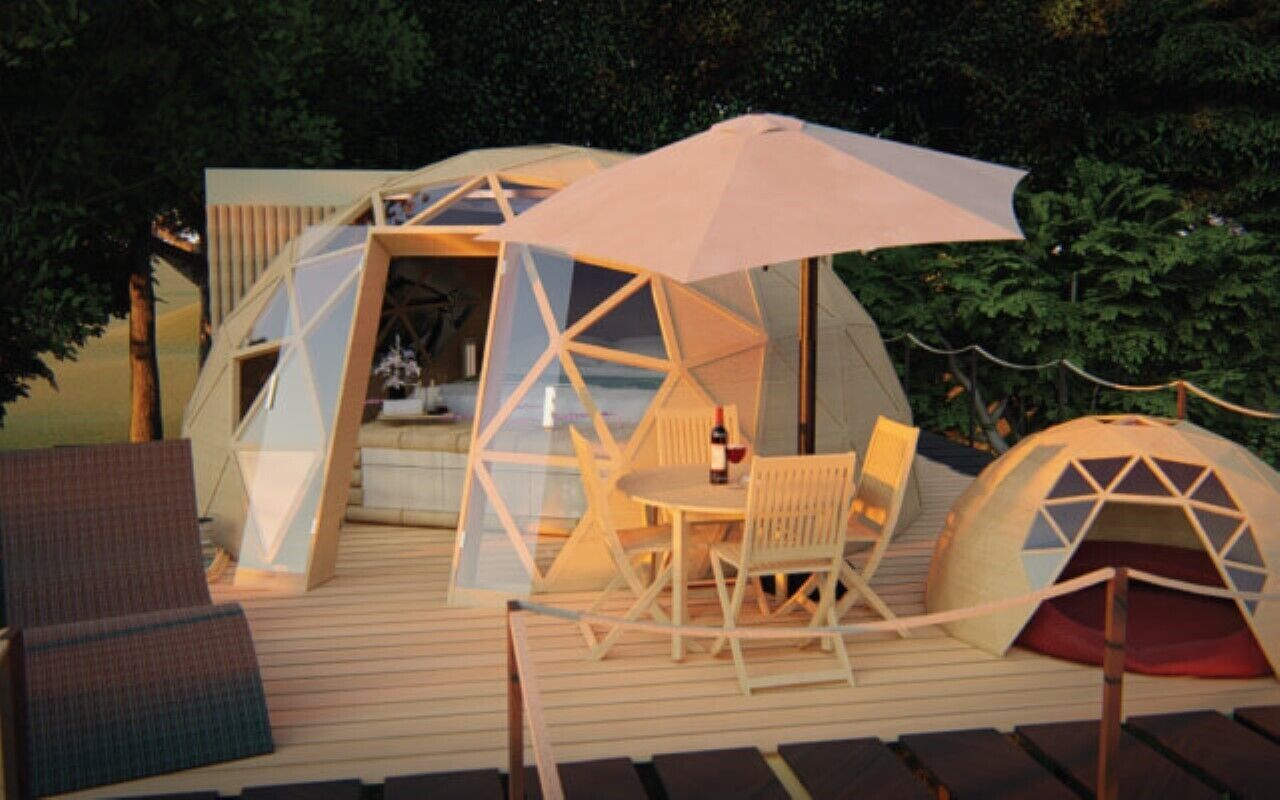 A geodesic dome structure with a table and chairs, surrounded by a deck and trees.