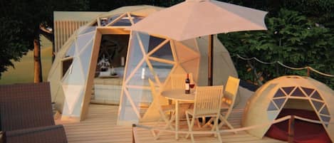 A geodesic dome structure with a table and chairs, surrounded by a deck and trees.
