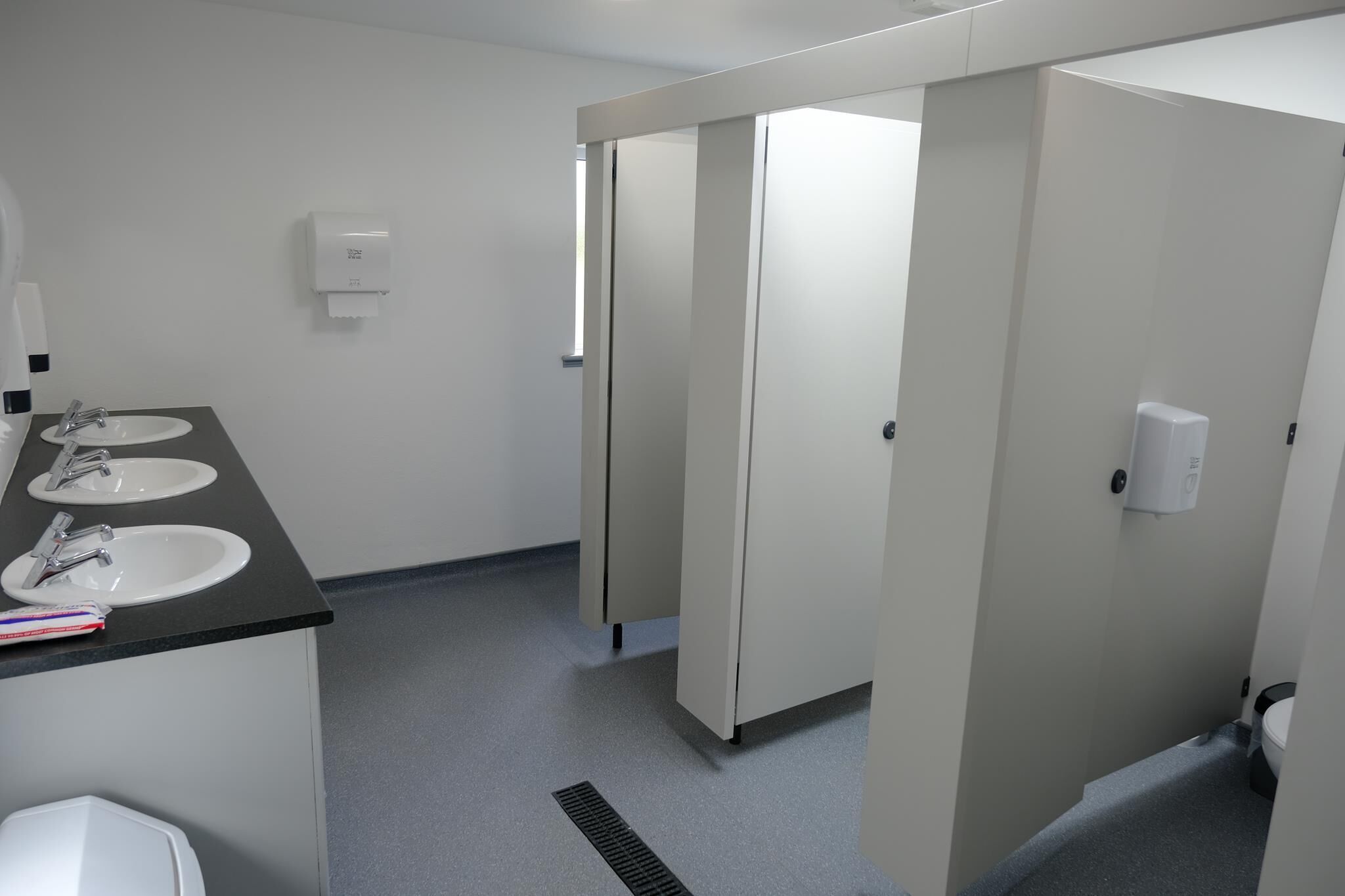A clean restroom with three sinks, a hand dryer, and a toilet.