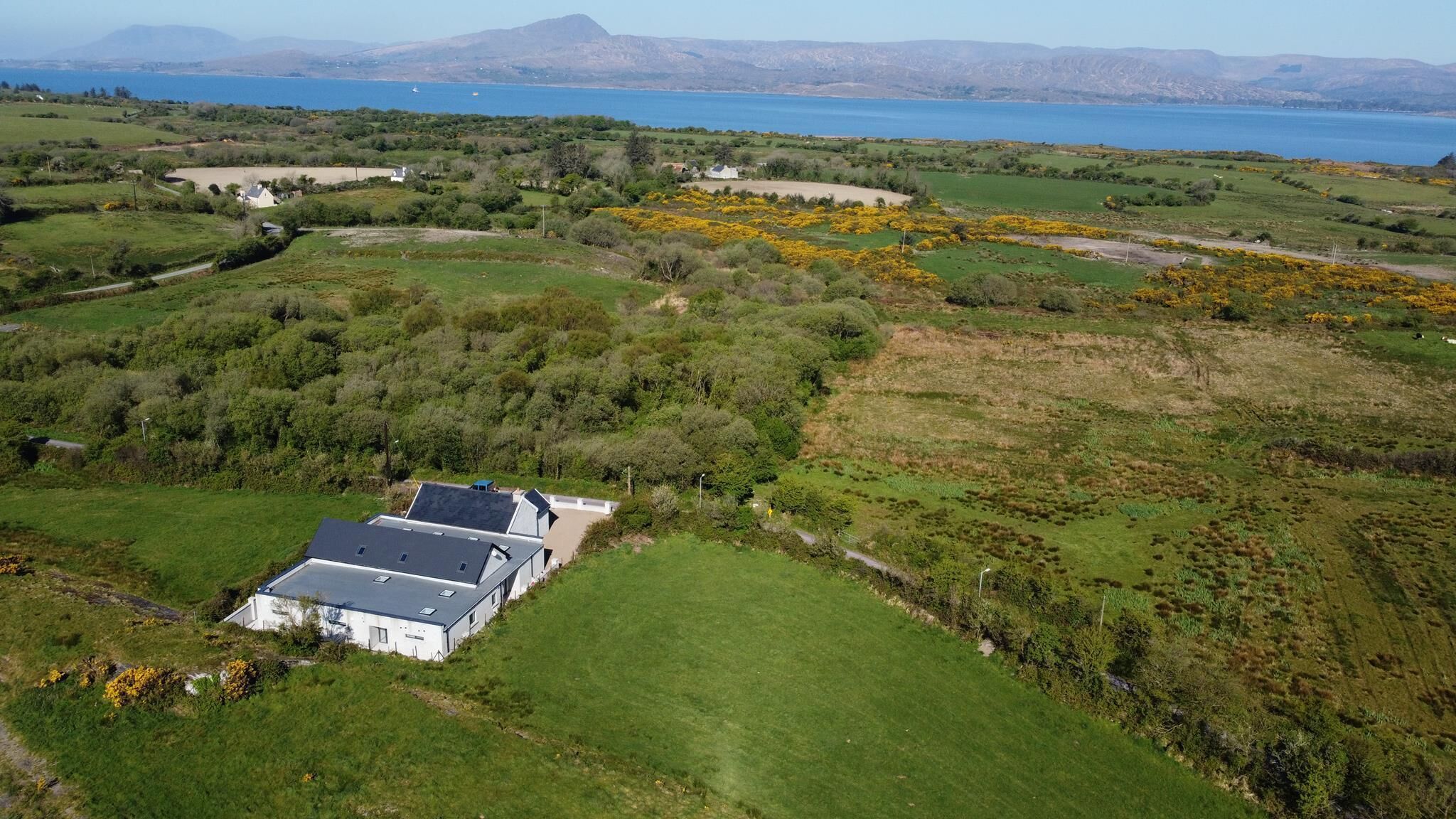 A rural landscape with a house surrounded by green fields and a body of water in the distance.