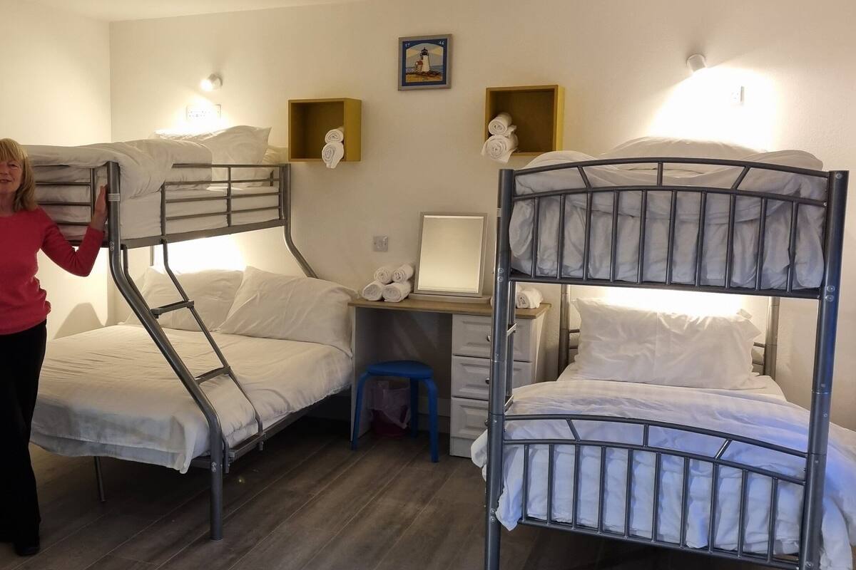 Un dormitorio con literas, un escritorio con silla y un taburete pequeño.
