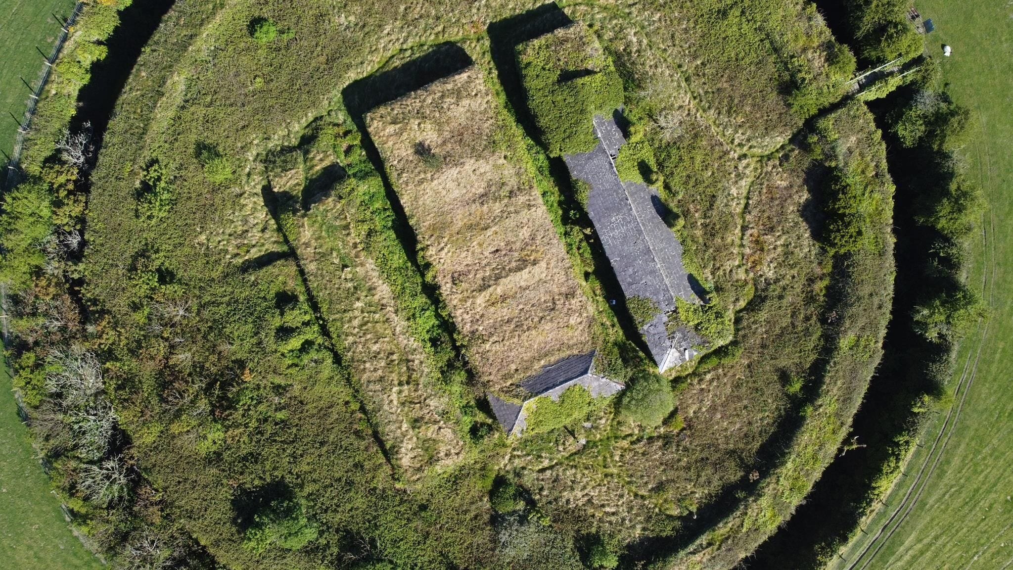 An aerial view of a rectangular building with a paved driveway, surrounded by grassy areas and trees.