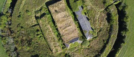 An aerial view of a rectangular building with a paved driveway, surrounded by grassy areas and trees.