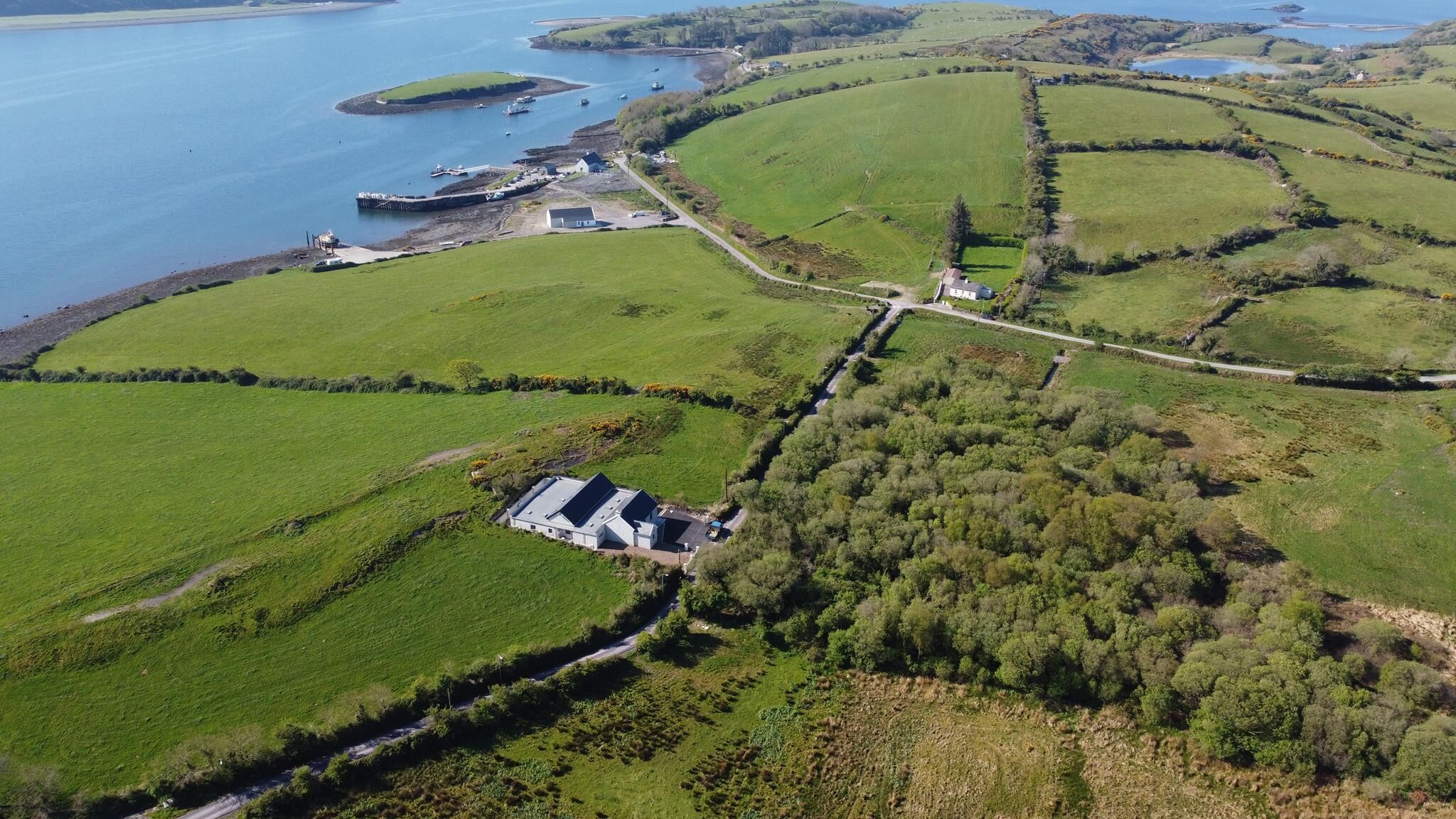Luchtbeeld van een kustgebied met velden, een steiger en een gebouw met schuin dak.