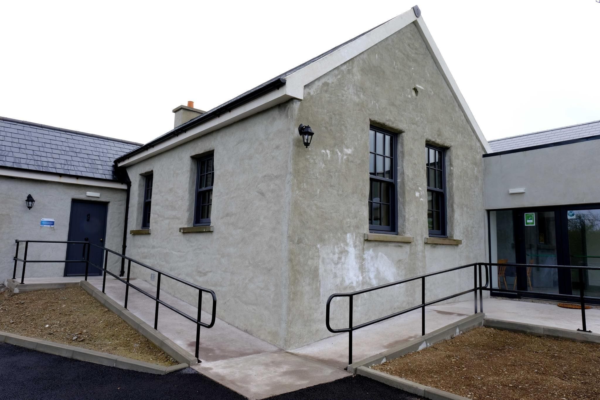 A building with a concrete facade, two windows, a door, and a small outdoor area with steps and railings.