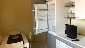 Una kitchenette compacta con un refrigerador Bosch, una pequeña mesa de comedor con sillas y un televisor sobre una encimera.
