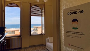Una habitación con vista al mar, un sofá blanco y un cartel en la pared sobre prevención de COVID-19.