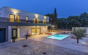 Une maison moderne à deux étages, dotée d’une piscine, d’un espace extérieur aménagé et d’un patio bien éclairé.
