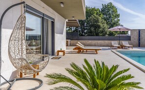 Un espace piscine extérieur moderne, doté de chaises longues, d’un fauteuil suspendu et d’une piscine.