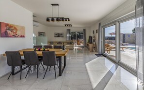 Un salon moderne avec un coin repas, de grandes fenêtres et une vue sur l’extérieur.