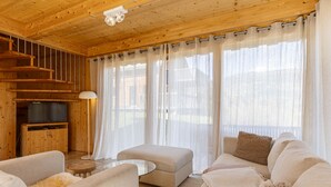 Een knus houten blokhut interieur met een bank, voetenbankje en een televisie op een houten kast.