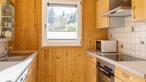Een keuken met houten kastjes, een raam, een magnetron en een fornuis.