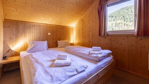 Dormitorio de cabaña de madera con dos camas, una mesita de noche y una ventana con cortinas.