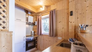 Una cocina compacta con paredes de madera, un refrigerador blanco, una estufa y un lavabo.