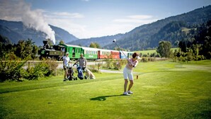 A golf course with a train in the background and mountains.