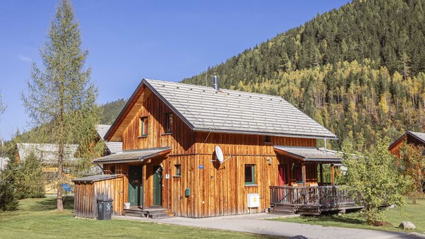 A wooden cabin with a porch and a satellite dish, surrounded by trees and a mountain backdrop. - Chalet # 139 with 4 bedrooms & whirlpool (Stadl an der Mur)