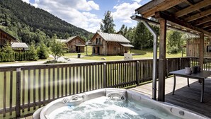 A hot tub on a wooden deck with a view of cabins and a forested mountain in the background.