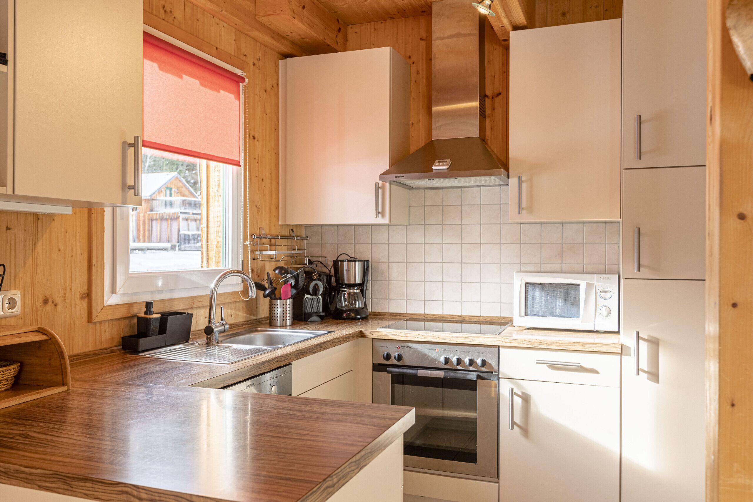 Une cuisine moderne avec des meubles en bois, une hotte en acier inoxydable, un four à micro-ondes et un lave-vaisselle.