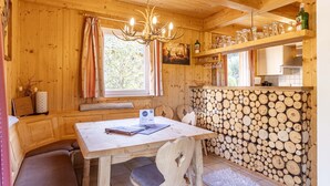 Interno di una baita in legno con un tavolo da pranzo, una panca, un lampadario e un muro di tronchi impilati.