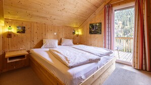 Camera da letto in una baita di legno, con un letto, comodini e vista su un balcone.