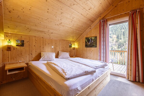 Une chambre dans une cabane en bois, avec un lit, des tables de chevet et une vue sur un balcon.