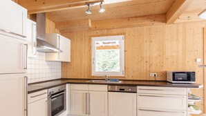 Una cocina moderna con paredes de madera, armarios blancos, horno de acero inoxidable, lavavajillas y microondas.
