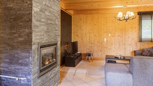 Een gezellige woonkamer met een open haard, houten wanden, een televisie en een bank.
