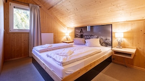 Een kamer met houten lambrisering, een groot bed, twee nachtkastjes en een raam met gordijnen.