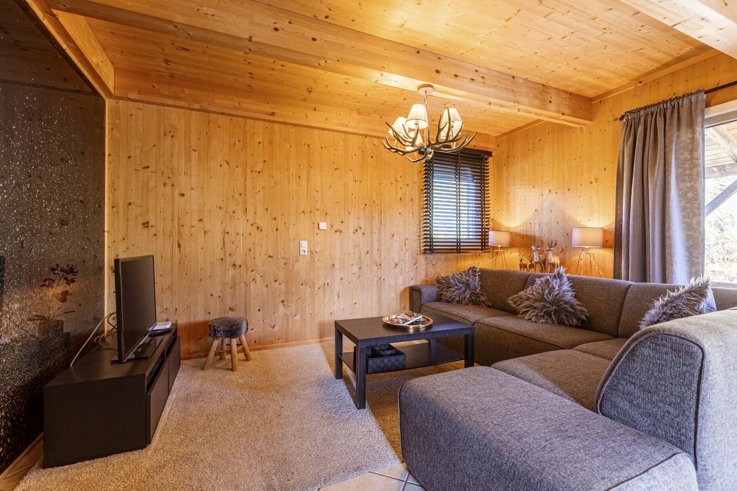 A cozy living room with wooden walls, a sofa, a coffee table, a TV, and a chandelier.