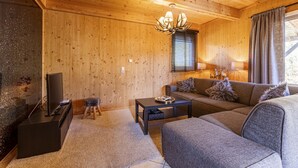 Een knus woongedeelte met houten wanden, een bank, een salontafel, een televisie en een kroonluchter.