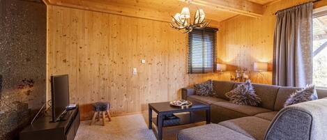 A cozy living room with wooden walls, a sofa, a coffee table, a TV, and a chandelier.