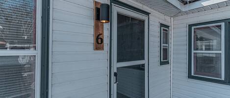 A white house with a wooden number sign, a black exterior light, and a sliding glass door.