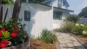 A white house with a 'Welcome' sign, a pathway, and various plants.