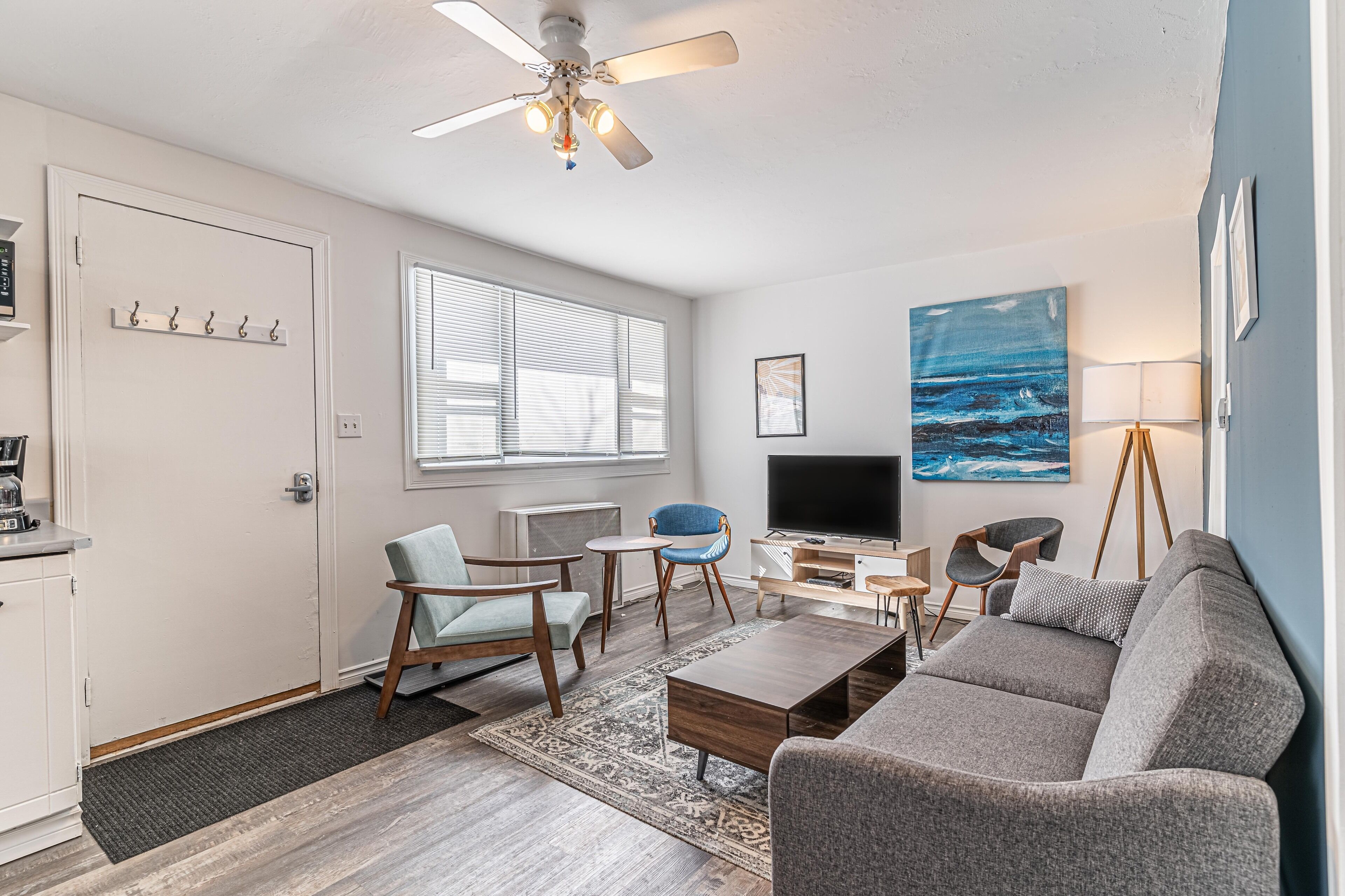 Un salon moderne doté d’un ventilateur de plafond, d’un téléviseur à écran plat, d’un canapé gris, d’un fauteuil bleu et d’une table basse.