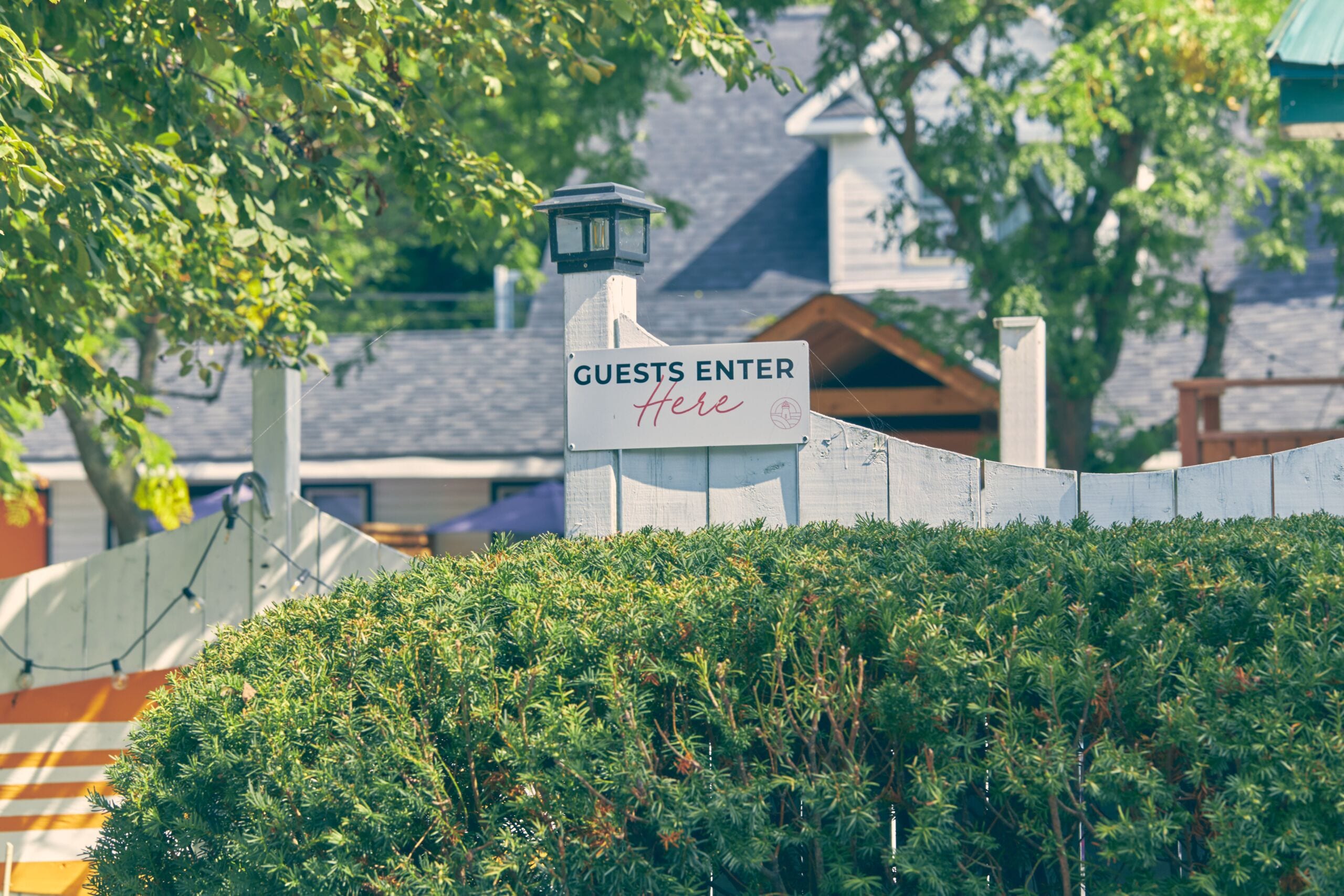 A sign indicating 'GUESTS ENTER Here' with a lamp post and a hedge in the foreground.