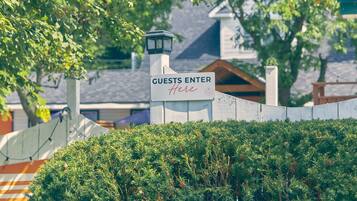 A sign indicating 'GUESTS ENTER Here' with a lamp post and a hedge in the foreground.