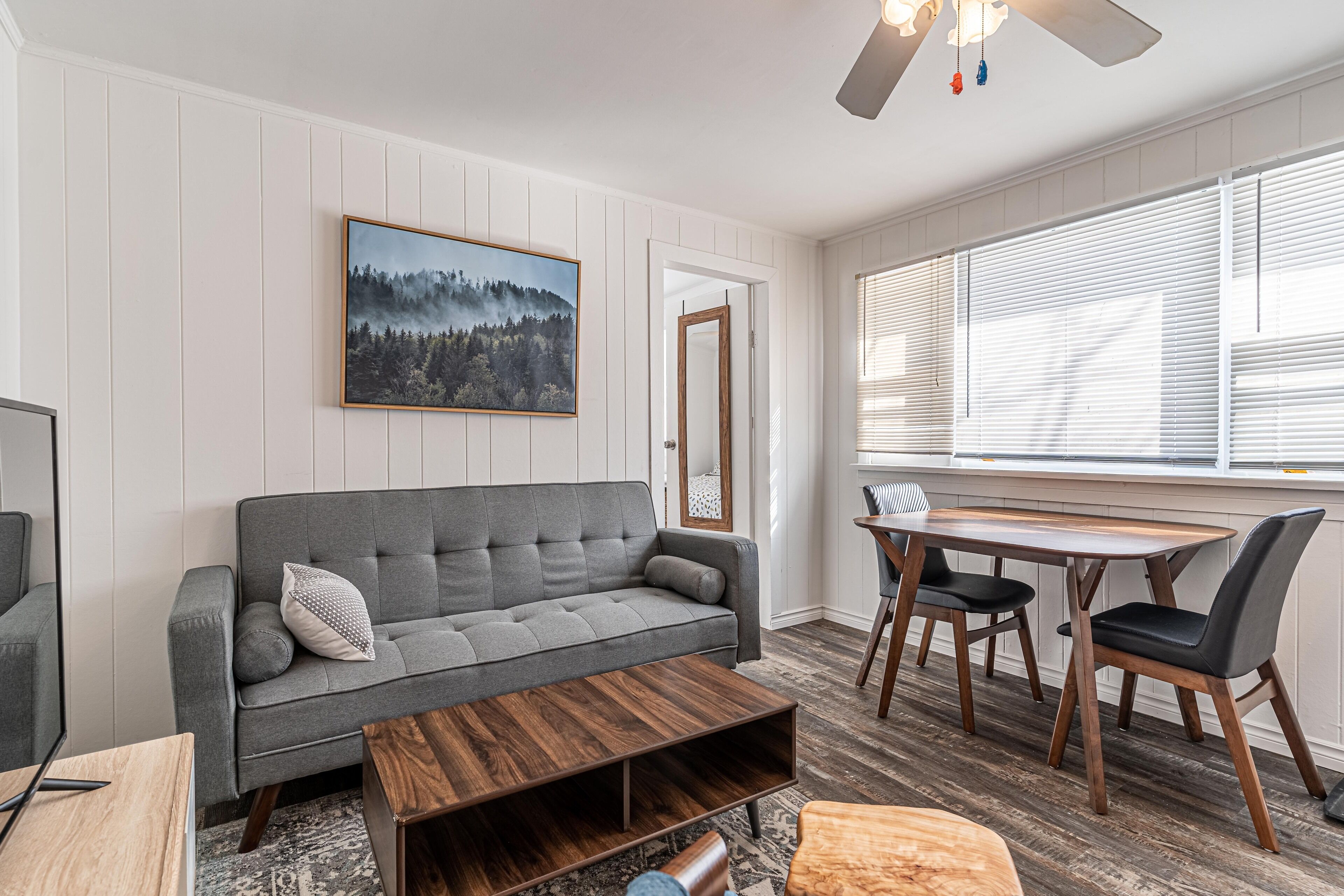 Ein Wohnzimmer mit grauem Sofa, einem Holztisch und einem Essbereich mit Holztisch und Stühlen.