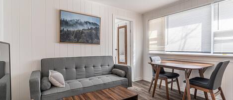 Ein Wohnzimmer mit grauem Sofa, einem Holztisch und einem Essbereich mit Holztisch und Stühlen.