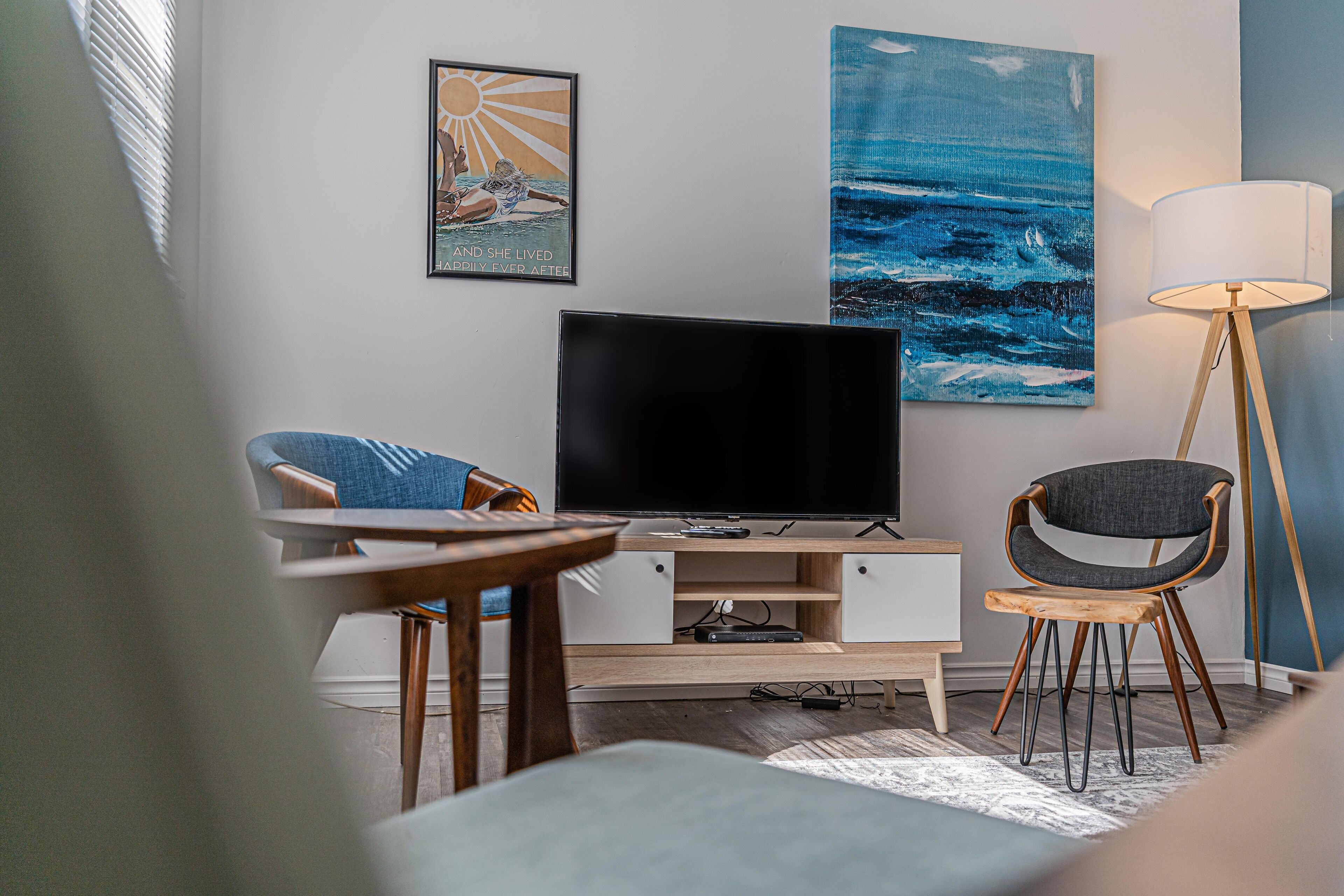 Un salón moderno con un televisor de pantalla plana, un cuadro de un océano azul y una lámpara de pie.