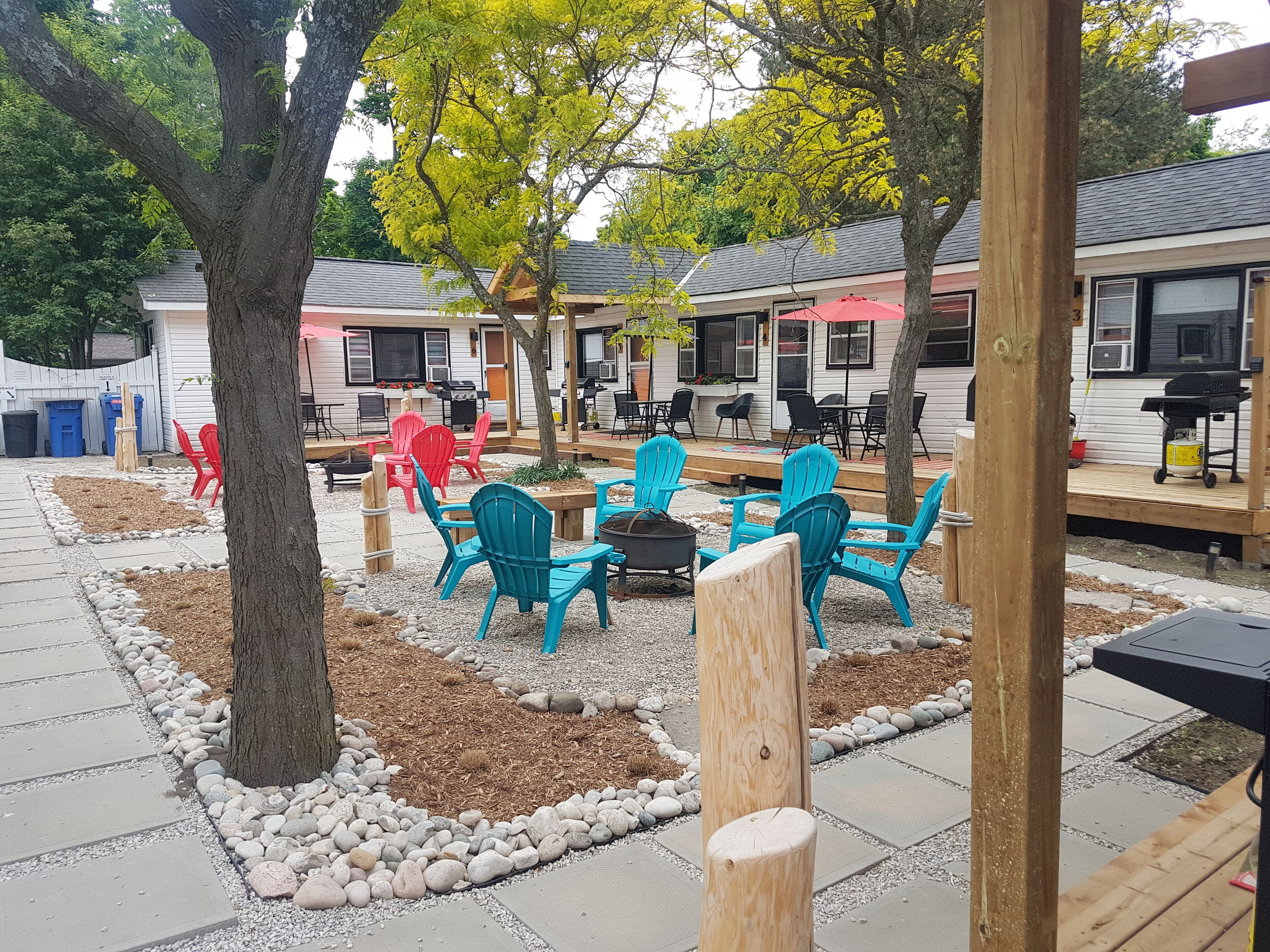 Un espace extérieur aménagé avec des chaises turquoise et un foyer, entouré d’un chemin de gravier et de poteaux en bois.