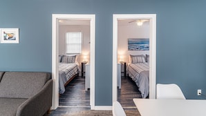 A room with two beds, a gray couch, and a white chair. - Driftwood Haus (Saugeen Shores)