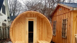 A wooden sauna with benches and a door, situated outdoors with a wooden structure nearby. - Driftwood Haus (Saugeen Shores)