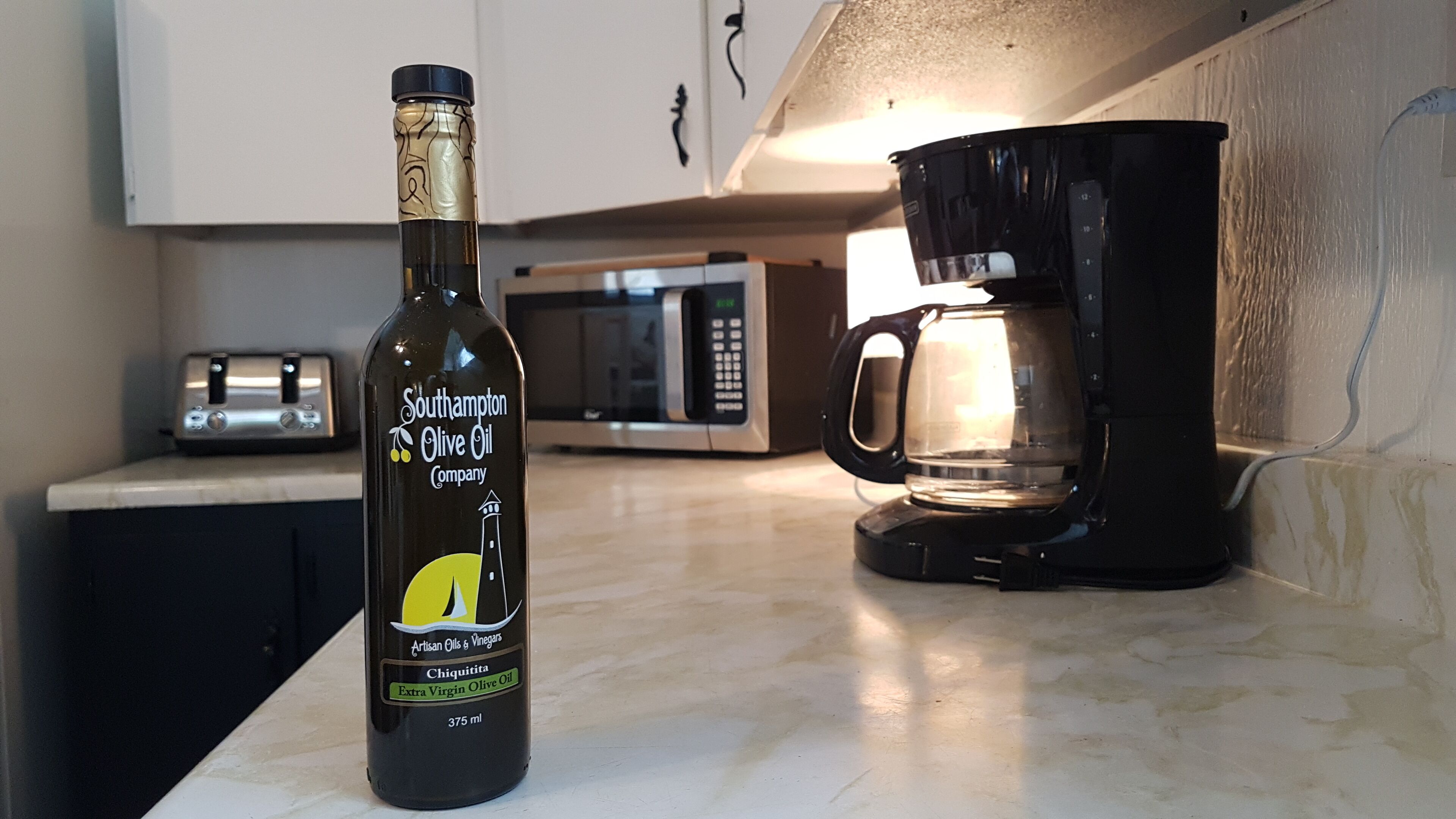 A kitchen counter with a bottle of Southhampton Olive Oil and a coffee maker.