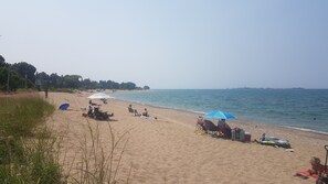 A beach with people relaxing under umbrellas, a few beach chairs, and a cooler on the sand.
