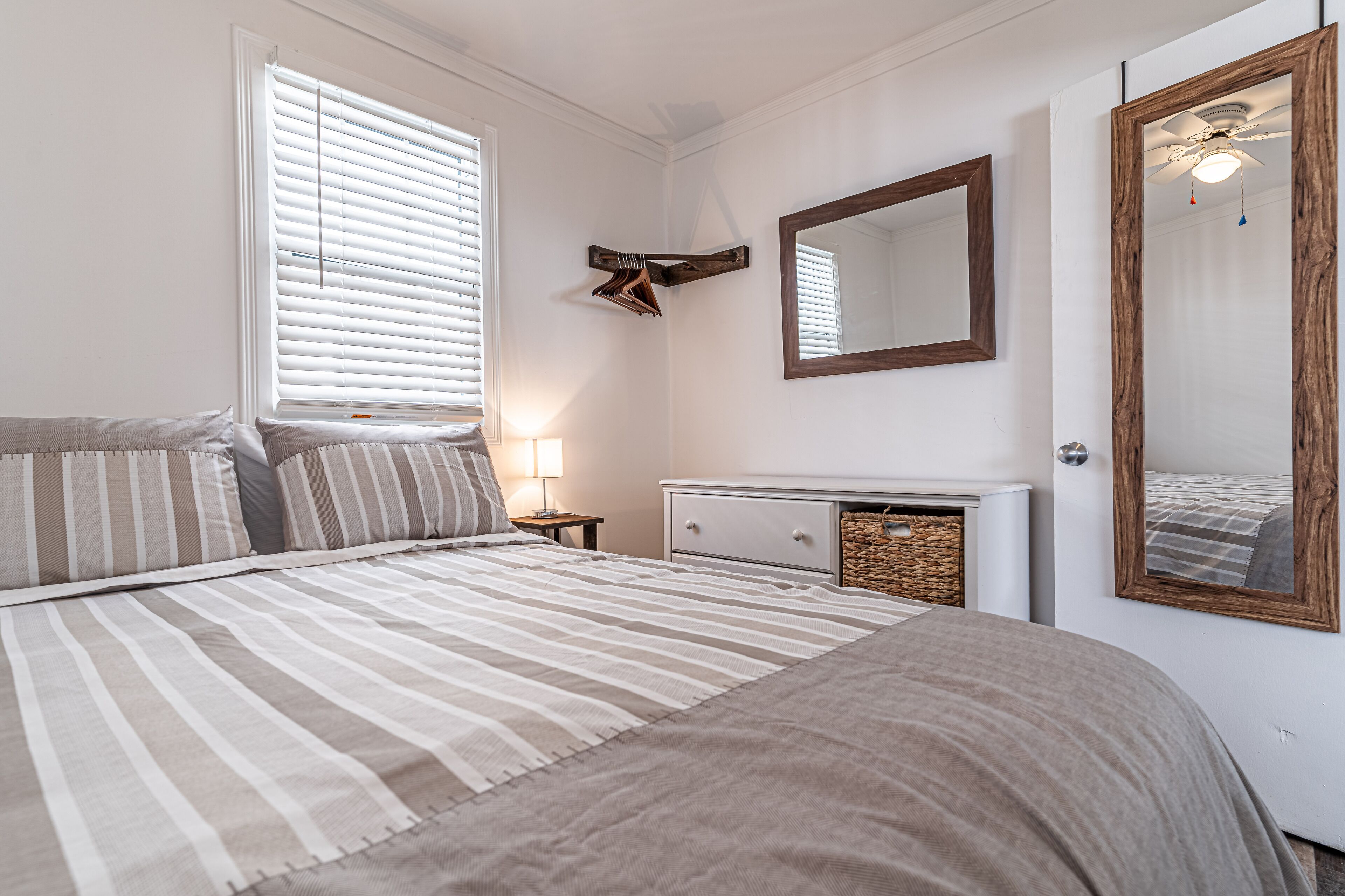 Ein Schlafzimmer mit einem Bett, einem Schminktisch, einem Spiegel und einem Fenster mit Jalousien.