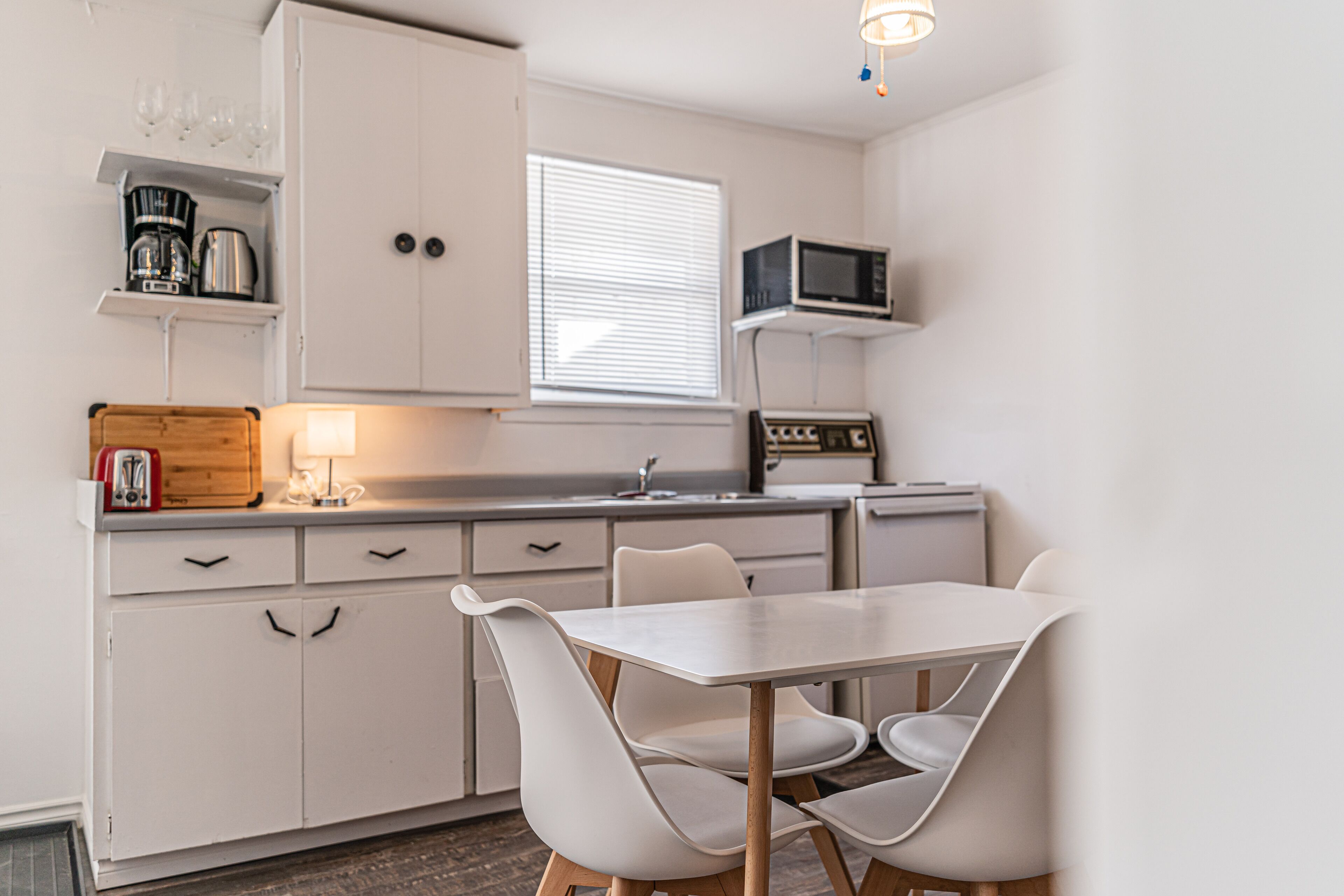 A compact kitchen with white cabinets, a dining table with chairs, a microwave, and a coffee maker on the countertop.