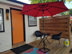 A wooden deck with a red umbrella, two black chairs, and a gas cylinder.