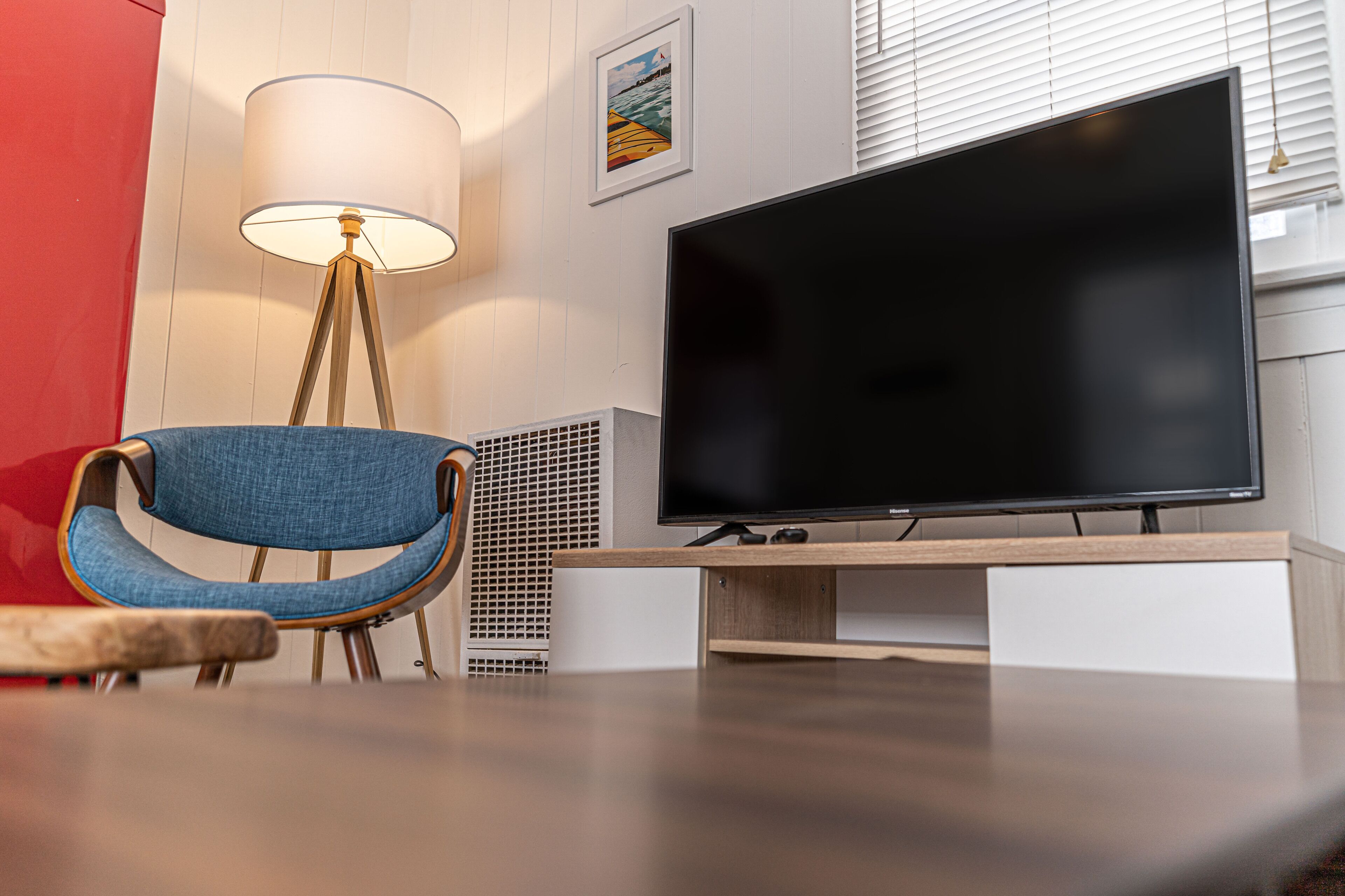 Una sala de estar moderna con televisor de pantalla plana, una butaca azul, una lámpara de pie y un cuadro en la pared.